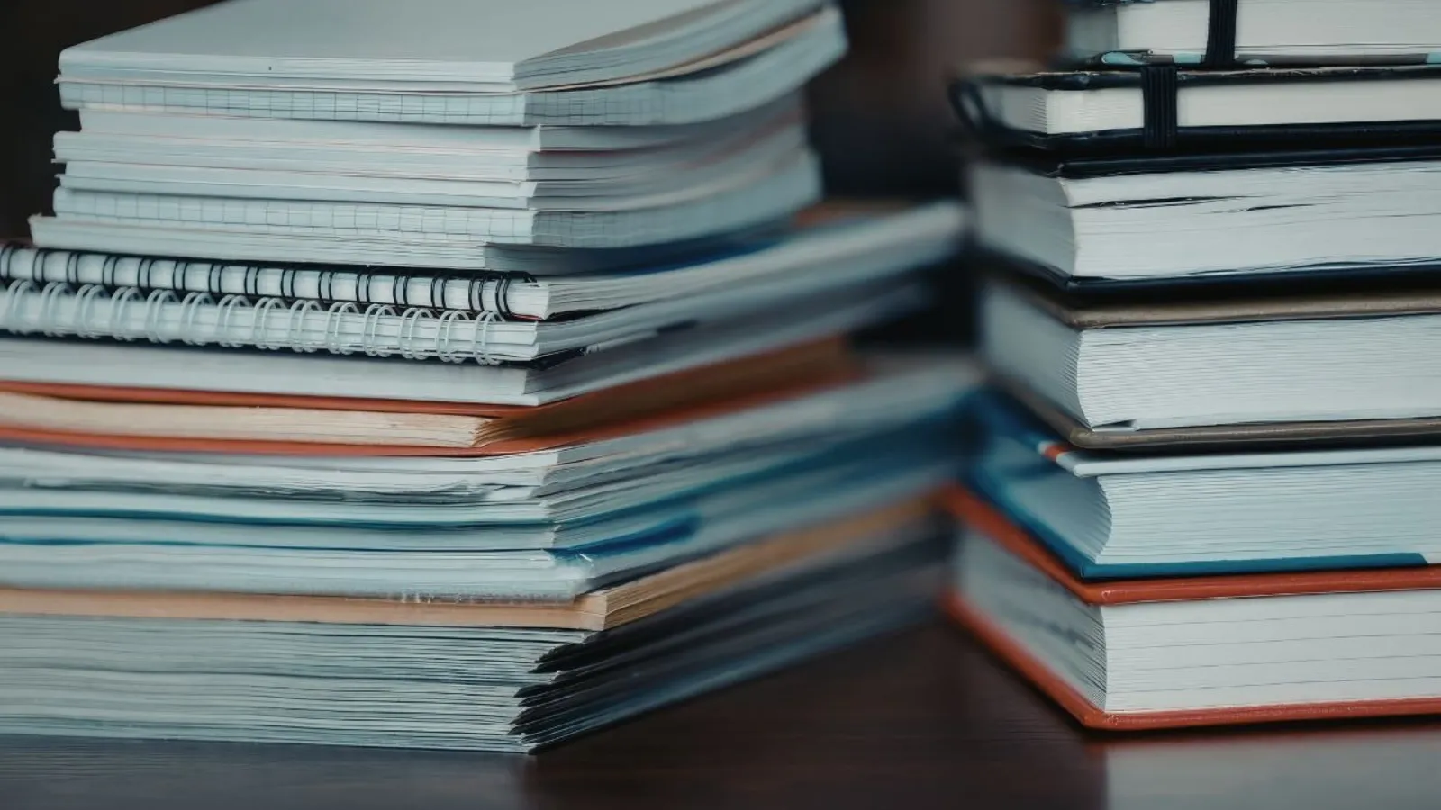 A stack of handwritten notebooks with pencilled margin notes, closed on a wooden desk.