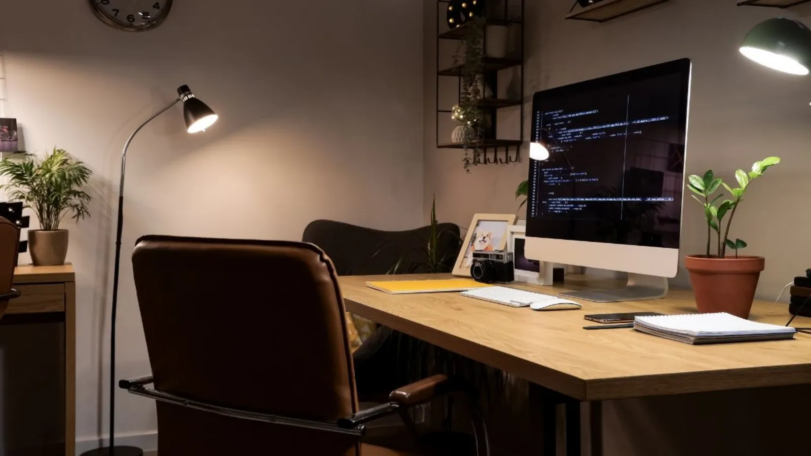 An empty desk in a dimly lit office at evening, chair turned away, one monitor still on.