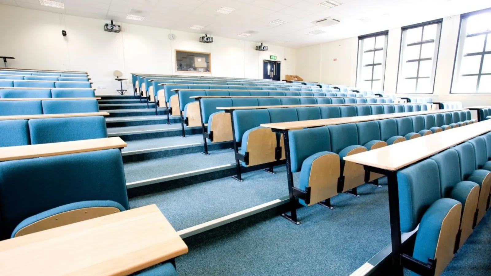 An empty tiered lecture theatre, rows of folding seats and writing desks with nobody in them.