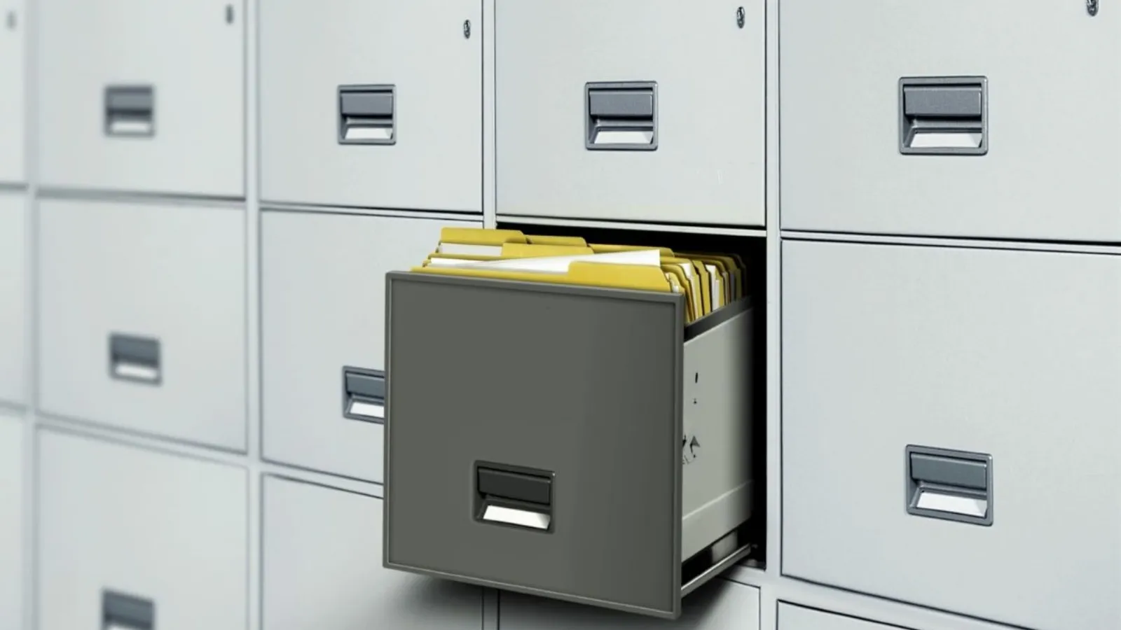 Grey metal filing cabinets, one drawer pulled open with yellow folders standing inside.