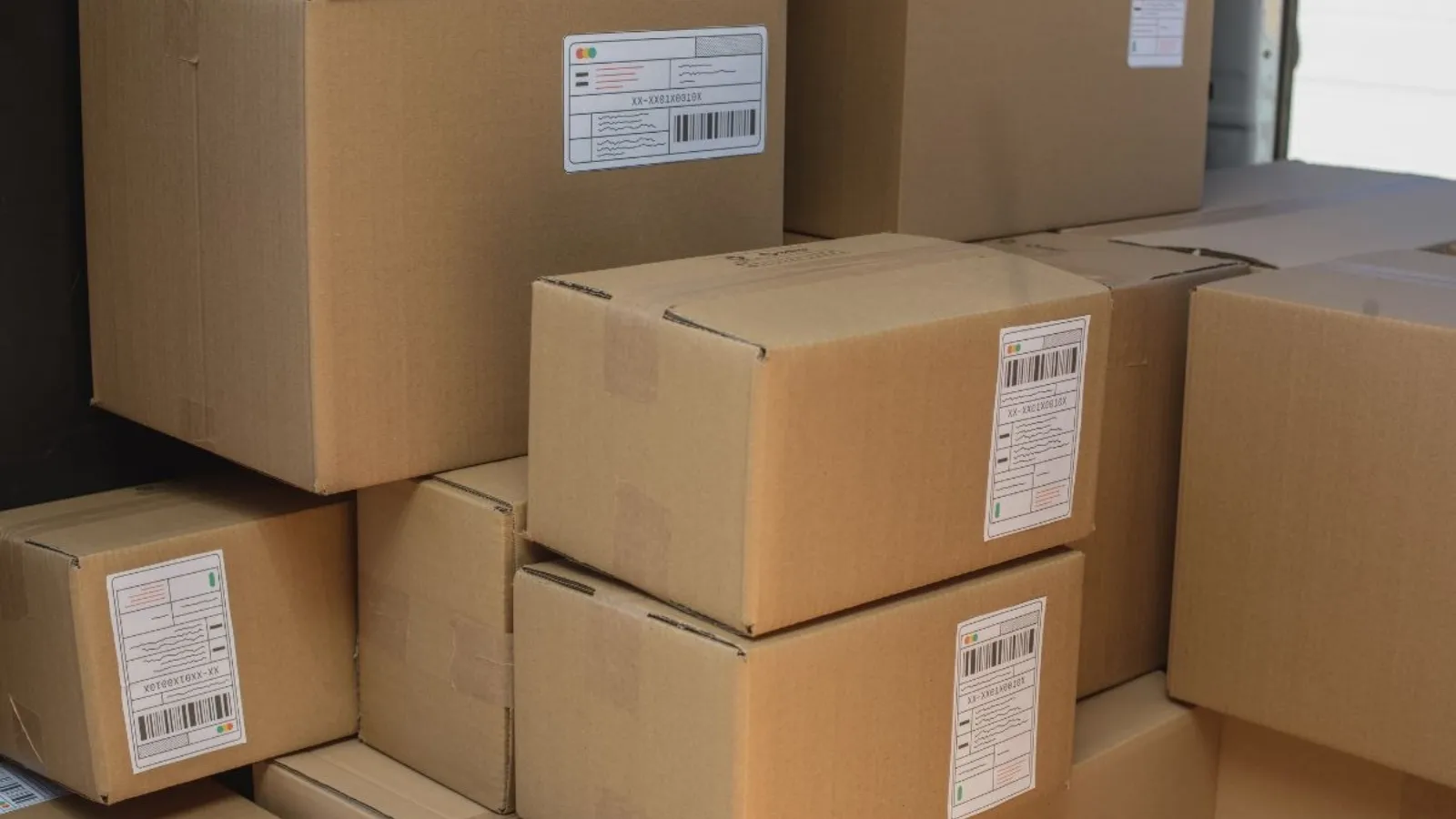 Stacked sealed cardboard boxes with printed shipping labels, waiting in a loading bay.