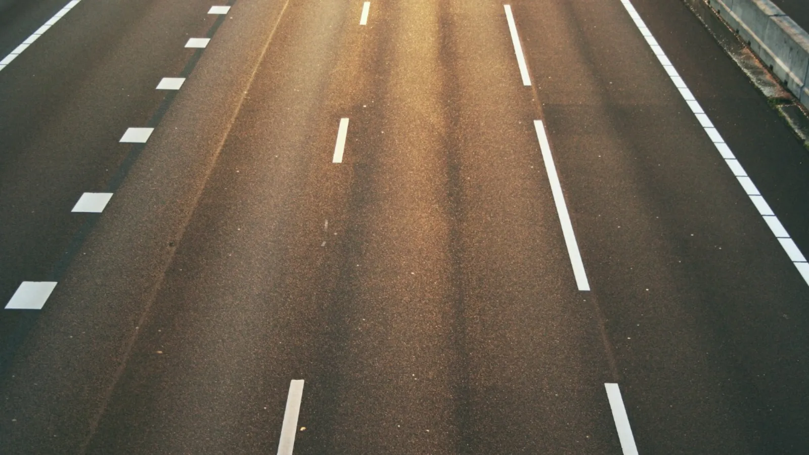 An empty multi-lane road photographed from above at dusk, white lane markings running away from the camera and no traffic in either direction.