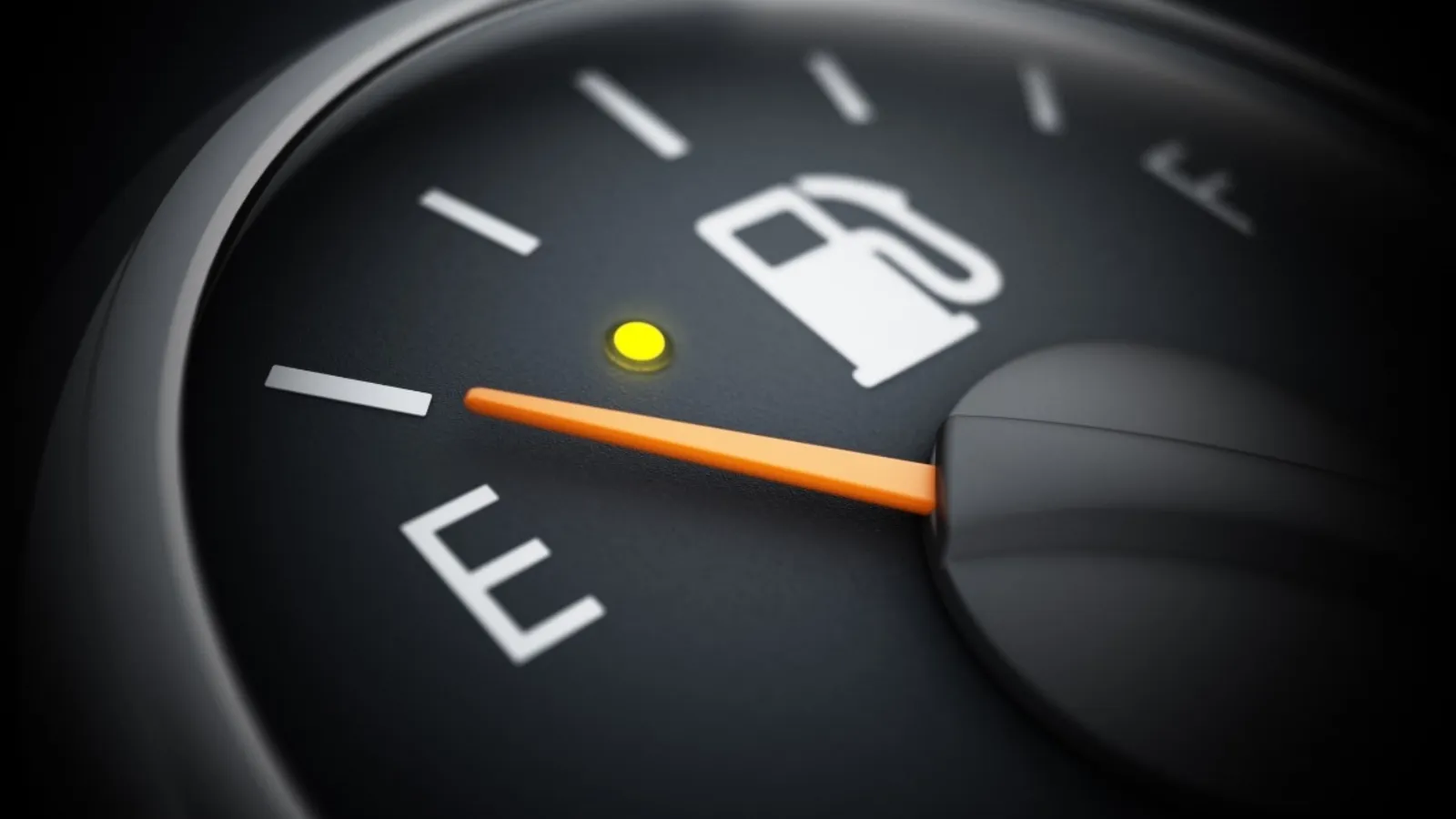 A car fuel gauge in close-up, the needle resting on empty with the low-fuel warning light lit.